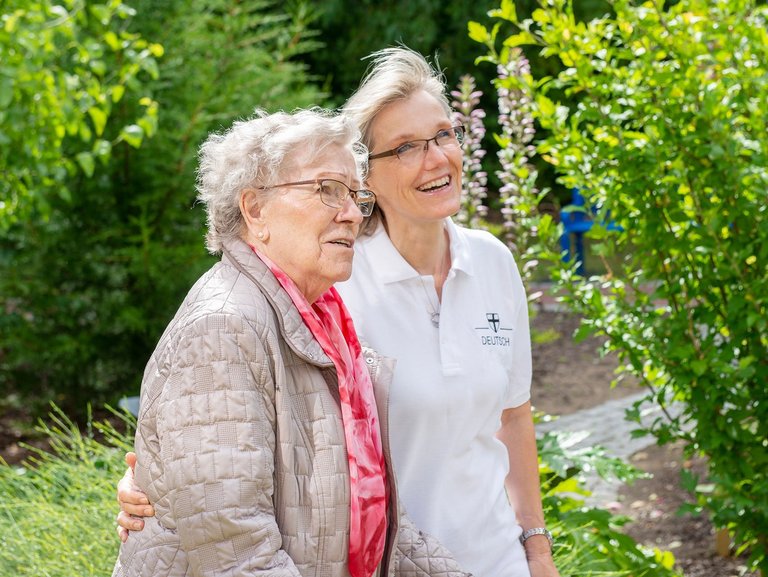 Im Garten: eine Pflegerin zeigt einer Bewohnerin etwas (nicht sichtbar)