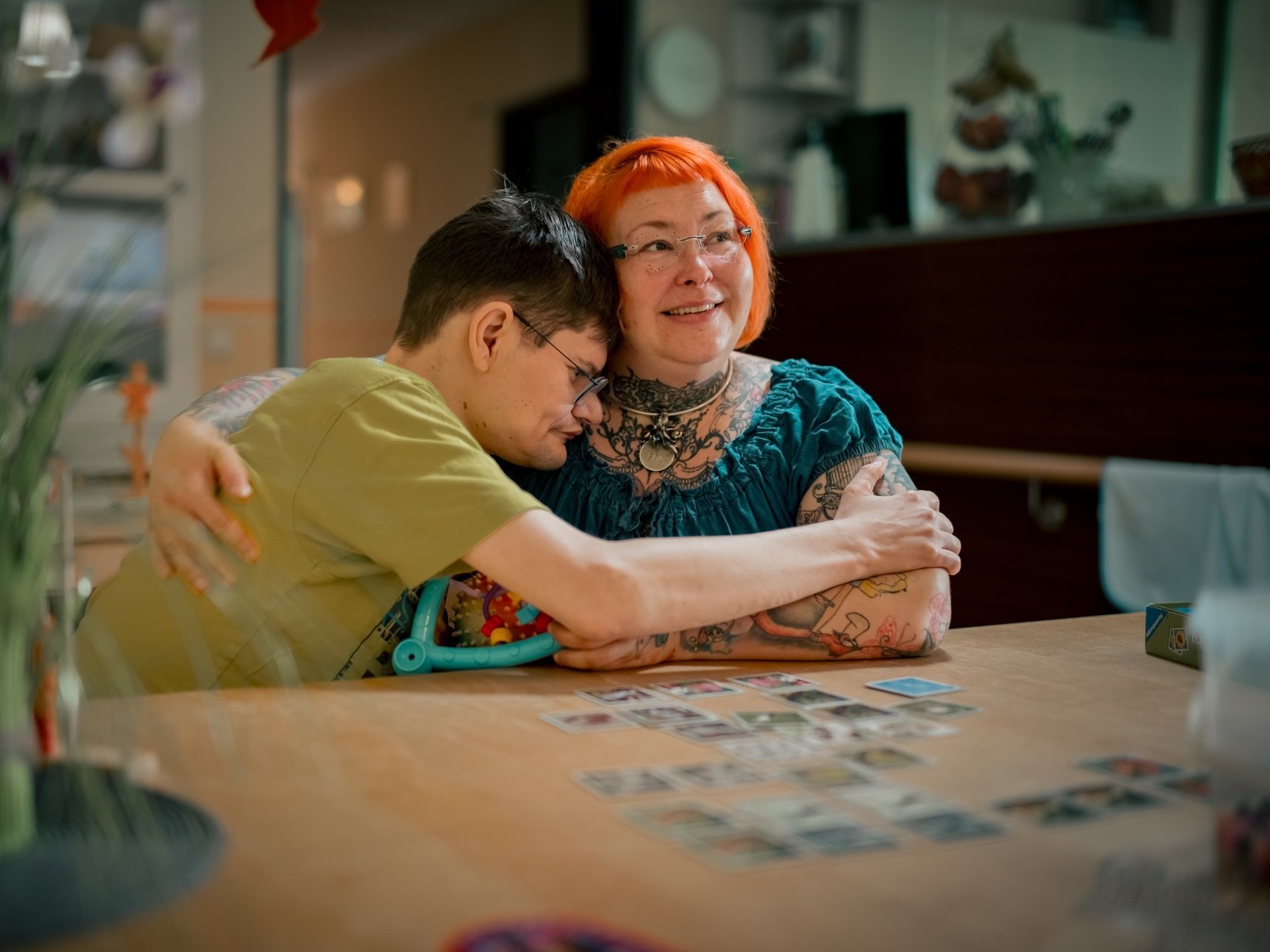 Eine Mitarbeitende und eine Person mit Beeinträchtigung umarmen sich und lächeln dabei.