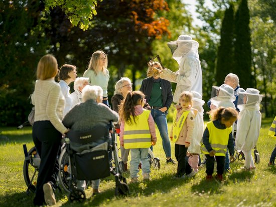 Eine Gruppe von Senioren und Kindern hat sich um den Imker versammelt, der allen etwas erklärt.